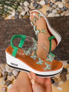 Detailed view of sparkling rhinestone butterfly embellishments on green platform wedge sandals
