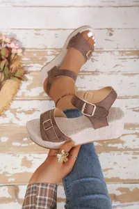 Close-up of brown buckled wedge sandals with textured platform and peep-toe design.