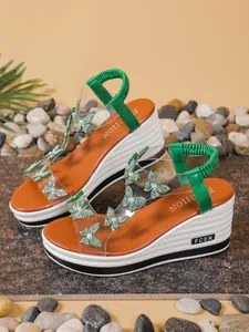 Close-up of the green rhinestone butterfly decorations on the transparent sandal straps.