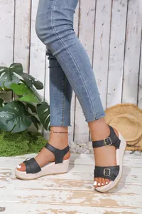 Detailed view of women's black buckle strap wedge platform sandals in a summer garden setting