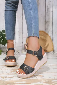 Detail view of black wedge sandals with gold buckles and a textured straw-like platform.