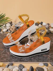 Detailed view of rhinestone butterfly decorations on clear strap wedge sandals