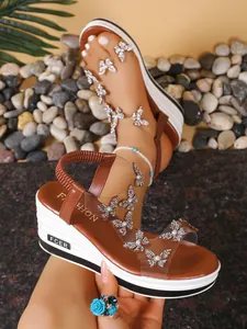 Close-up of brown wedge sandals with sparkly rhinestone butterflies and clear straps