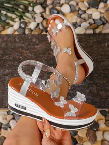 Detailed view of sparkling rhinestone butterfly accents on transparent wedge sandals.