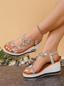 Close-up of silver wedge sandals with rhinestone butterflies and transparent straps.