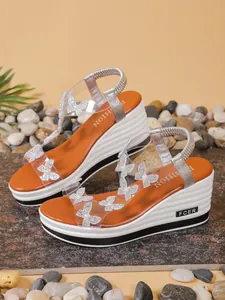 Close-up of rhinestone butterfly details on transparent strap wedge sandals