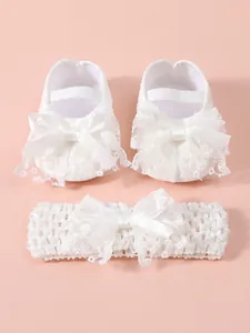 Close-up detail of white lace baby shoes and matching bow headband set for newborns