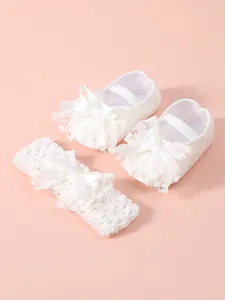 Close-up detail of elegant white lace baby shoes and matching headband set for newborns.