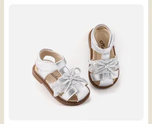 Close-up of silver baby girl sandals with lace bows and soft brown soles