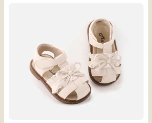Top-down view of cream baby girl sandals featuring lace bow details and soft brown soles.