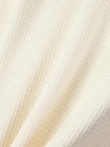 Macro view of premium cream waffle knit fabric showing detailed grid texture and soft feel