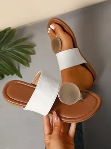 Detailed view of white croc-embossed thong sandals with a large gold metal disc