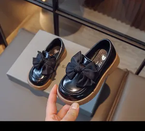 Gros plan montrant le grand nœud décoratif sur les mocassins en cuir noir pour filles