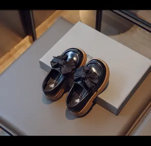 Gros plan de mocassins en cuir noir pour filles avec un grand nœud et semelle épaisse