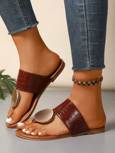 Detail view of brown crocodile-embossed thong sandals with gold metal disc ornament