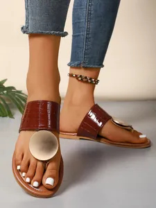 Detailed on-foot view of brown crocodile-embossed thong sandals with gold metal disc