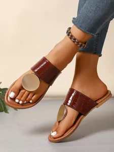 Detail of brown crocodile-embossed thong sandals with large gold metal disc ornament