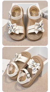 Detailed view of elegant girls' white summer sandals with rhinestone bow accents.