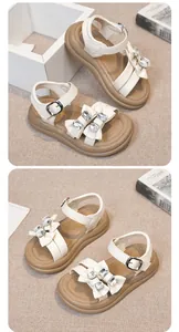Detail view of white girls sandals featuring glittering rhinestone bows and tan soles