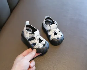Vue détaillée de sandales pour bébé blanches et noires tenues à la main par un adulte