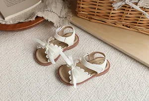Vue détaillée de sandales crème pour filles avec bordure en dentelle et nœuds blancs