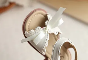 Gros plan de sandale pour fille avec nœud en ruban crème et détails en dentelle.