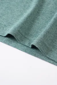 Gros plan des coutures de l'ourlet à double aiguille sur un t-shirt en coton vert.
