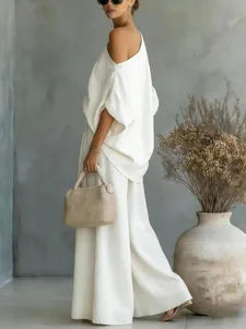 Model wearing chic white off-shoulder top and wide-leg pants set in minimalist studio