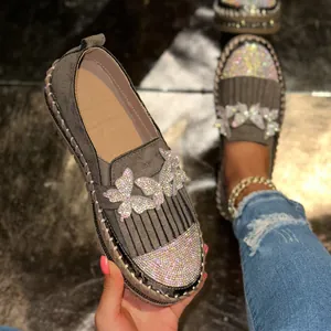Nahaufnahme grauer Wildleder-Loafer mit Fransen und funkelnden Strass-Schmetterlingen.