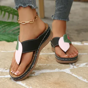 Primer plano de chanclas con cuña para mujer con motivos de hojas sobre piedra.
