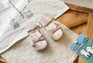 Detailed top view of pink floral girls' sandals with bow straps on a rustic setting.