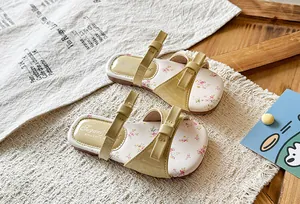 Close-up detail view of elegant girls' cream sandals with bowtie and floral insoles.
