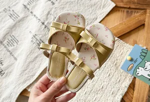 Detail view of girls' bow-knot sandals with floral print insoles on wooden background.