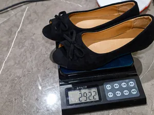 Weight measurement of black suede flat shoes with bow, showing 292.2g on scale.