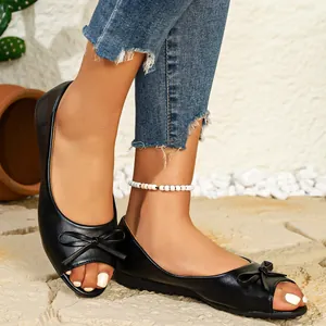 Detailed view of black flat peep-toe shoes with bow detail on a model's feet outdoors