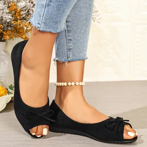 Close-up of black suede peep-toe flats with bow detail worn with jeans.