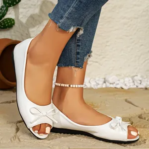 Close-up of white peep-toe flat shoes with elegant bow details on a model's feet.