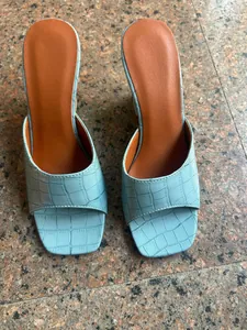 Vue de dessus détaillée des mules bleu clair à motif crocodile et bout carré sur sol.