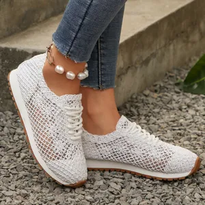 Detail of breathable white lace mesh sneakers with lace-up design worn on outdoor gravel surface.