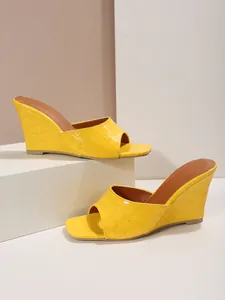 Vue latérale de sandales compensées jaunes motif crocodile sur un fond minimaliste