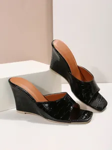 Vue latérale de sandales compensées noires effet croco avec une finition vernie brillante.