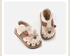 Detailed view of beige baby girl closed-toe walking sandals with heart cutout and plaid bow
