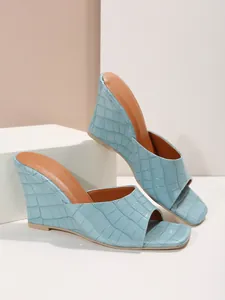 Gros plan de sandales compensées bleu clair avec texture crocodile embossée et bout ouvert.