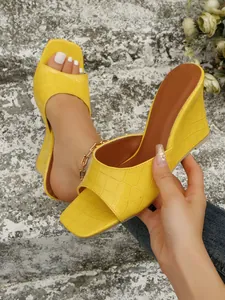 Détail de sandales compensées jaunes avec texture crocodile et bride unique.
