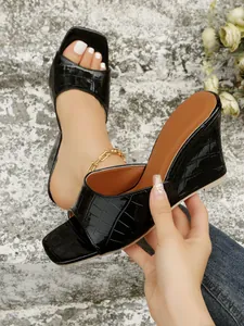 Détail de sandales à talons compensés noirs gaufrés croco avec un bout carré élégant.