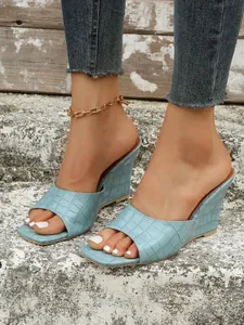 Vue rapprochée de sandales compensées bleu clair à texture crocodile sur un mannequin.