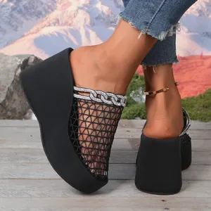 Detail van zwarte sleehak-muiltjes met mesh en strass-kettingversiering.