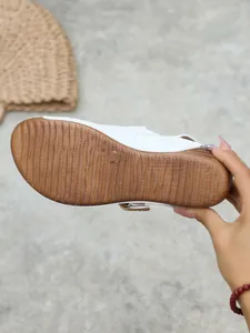 Detailed view of the brown textured non-slip sole of a white wedge sandal