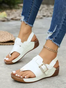 Close-up of white wedge sandals featuring a sparkling rhinestone buckle and toe-loop