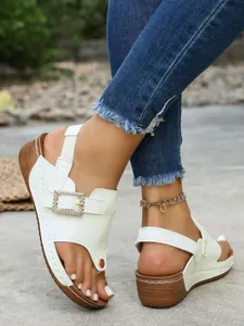 Detail shot of white wedge sandals with rhinestone square buckle and clip-toe design
